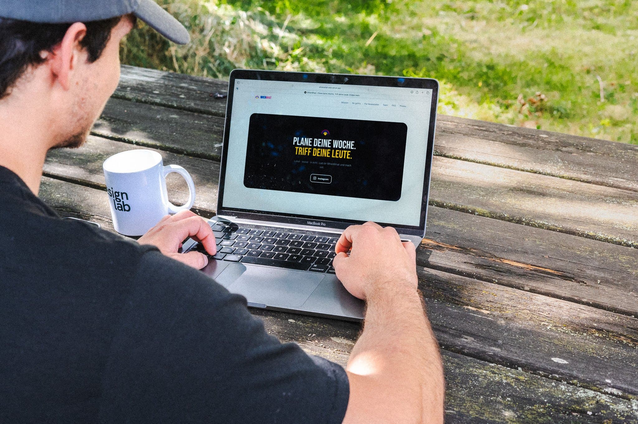 Person plant am Laptop an einem Holztisch im Grünen